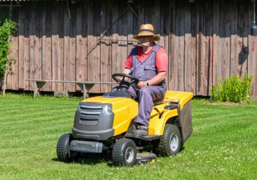 a senior man with a lawn mower mows the grass in the yard of country house
